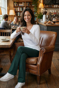 Woman in white long-sleeve tee and green lounge pants relaxing with coffee in cozy cafe