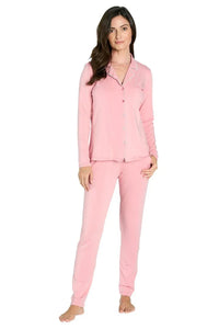 Woman wearing light pink long sleeve button-up pajama set with pants, standing barefoot