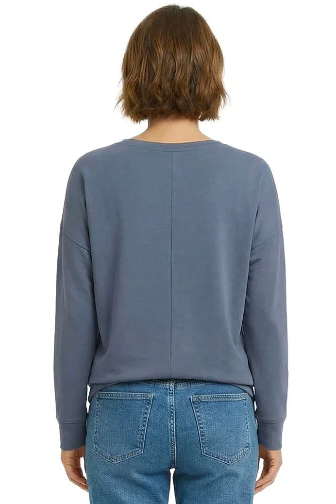 Woman wearing steel blue long sleeve lounge top and blue jeans, shown from the back