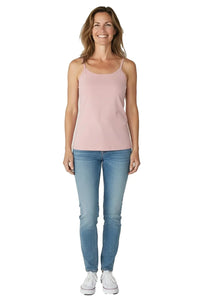 Smiling woman wearing shell pink camisole top, light blue jeans, and white sneakers on white background