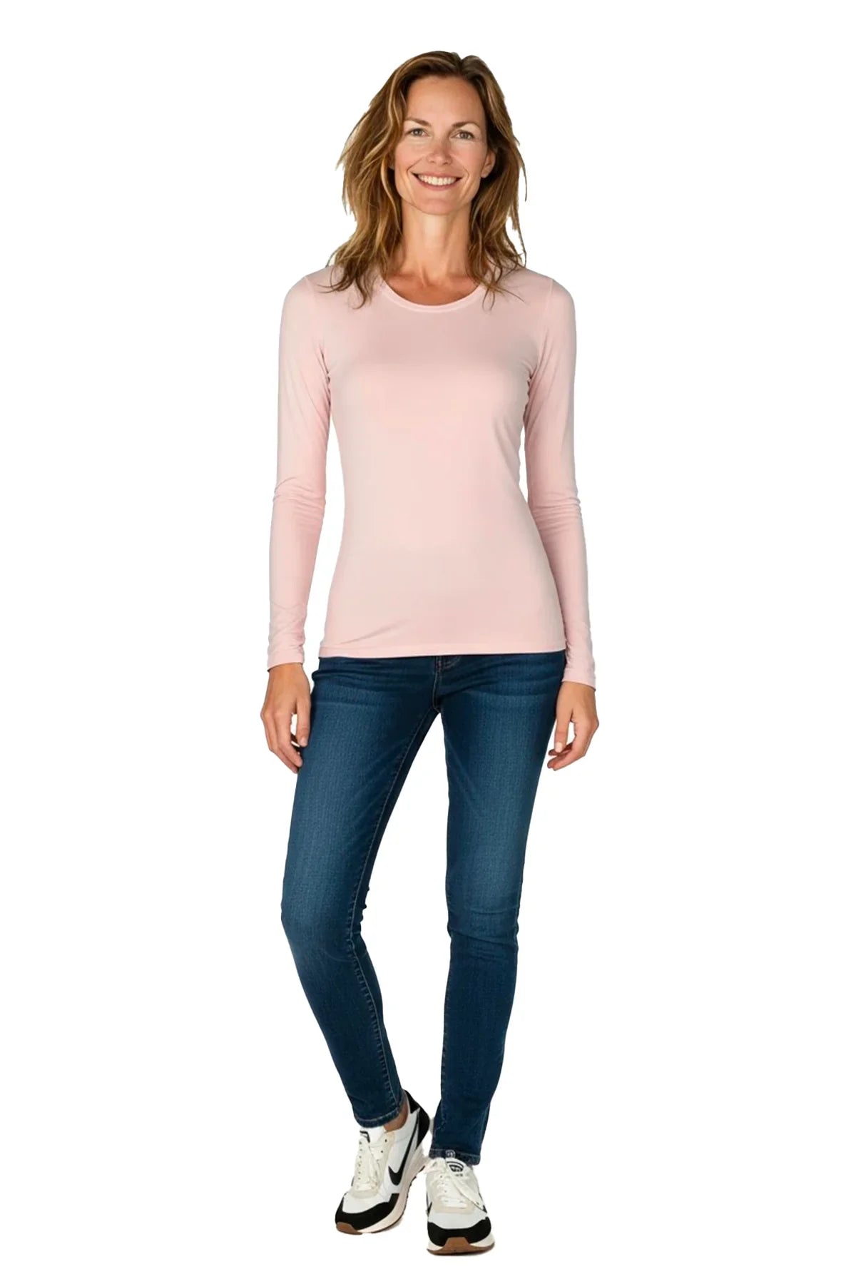 smiling woman wearing shell pink long sleeve shirt with blue jeans and white sneakers