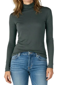 Woman wearing dark green turtleneck long sleeve top paired with blue denim jeans