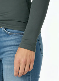 Close-up of a person wearing a spruce green long sleeve top paired with light blue denim jeans