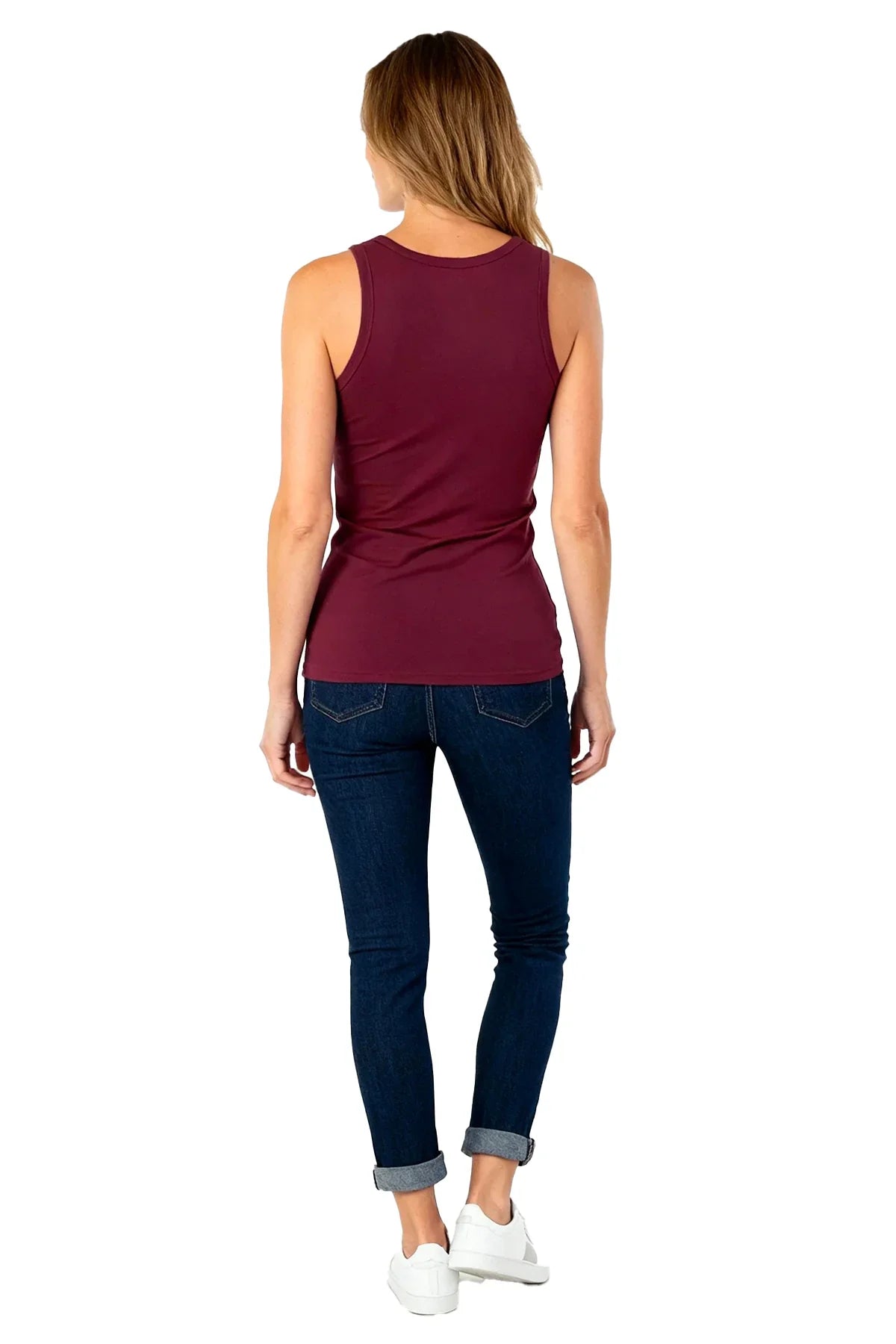 Rear view of woman wearing a fitted burgundy tank top, dark blue rolled-up jeans, and white sneakers