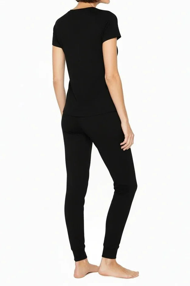 Woman wearing black short-sleeve top and black fitted pants standing barefoot on white background